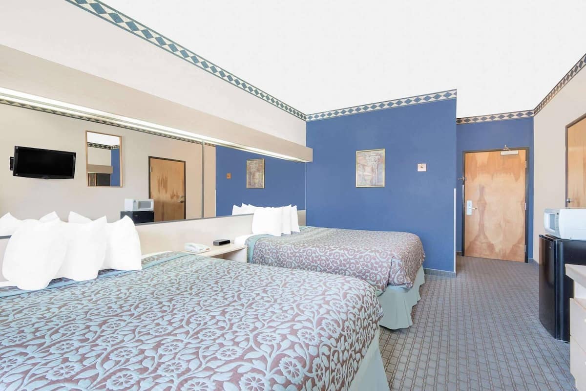 Een hotelkamer met twee bedden, een grote spiegel, een flatscreen televisie, een bureau met een magnetron, en een deur naar een andere kamer.