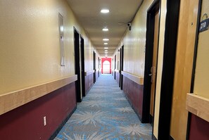 Un couloir d’hôtel avec des portes des deux côtés, un sol recouvert de moquette et un plafond doté d’un éclairage encastré.