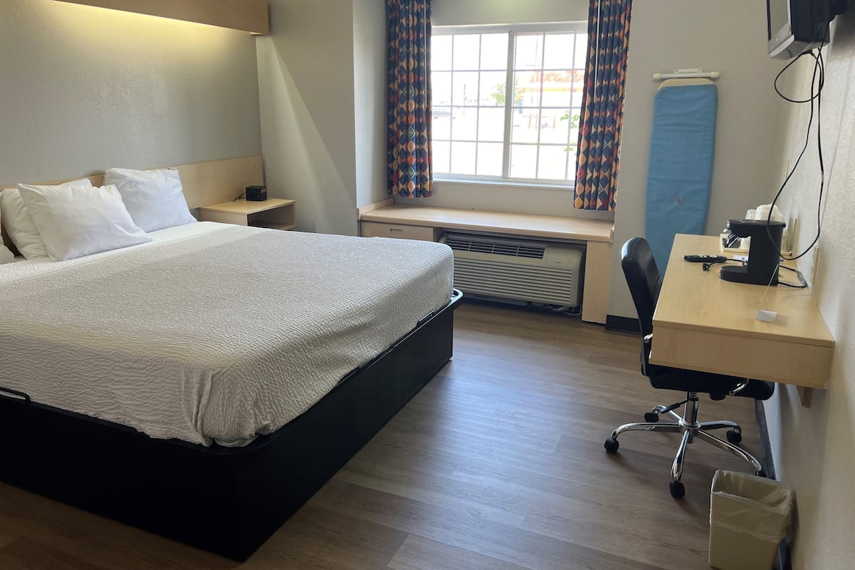 Een hotelkamer met een bed, nachtkastje, bureau, stoel en een raam met gordijnen.