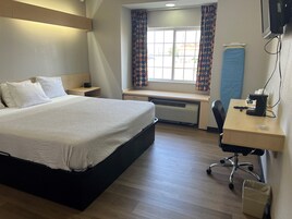 Quarto de hotel com cama, mesa de cabeceira, escrivaninha, cadeira e janela com cortinas.