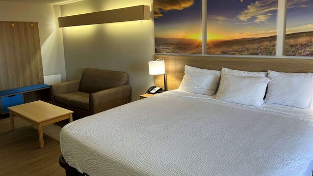 A hotel room with a large bed, a desk, a chair, and a nightstand with a lamp.