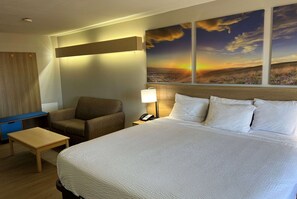 Habitación de hotel con una cama grande, un escritorio, una silla y una mesita de noche con lámpara.