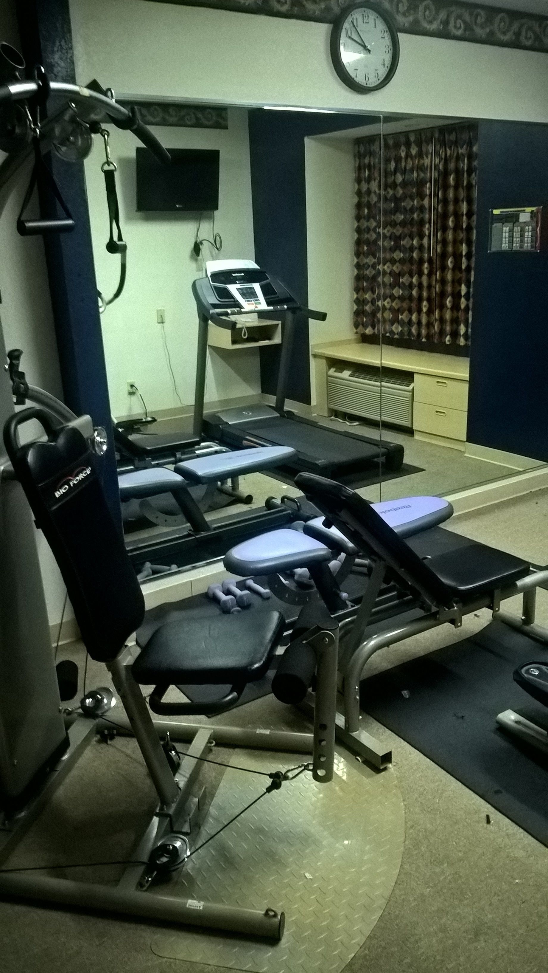 A gym with exercise equipment, a clock, and a desk with a computer.