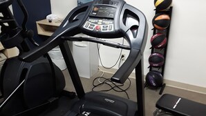 A treadmill in a room with a water bottle, a bench, and exercise balls.