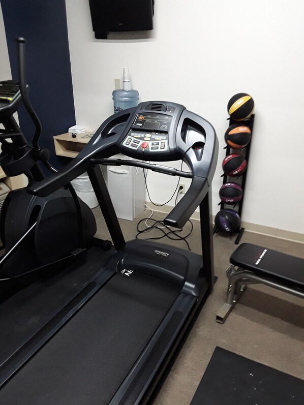 A treadmill in a room with a water bottle, a bench, and exercise balls.