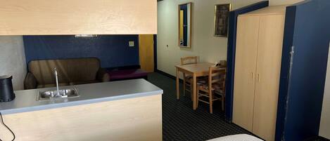 A compact hotel room with a kitchenette, a bed, a desk, and a wardrobe.