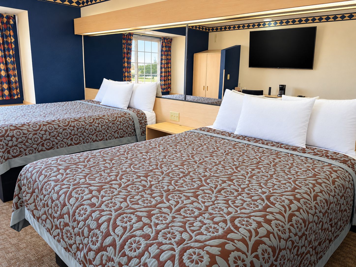 Quarto de hotel com duas camas, televisão, escrivaninha e guarda-roupa.