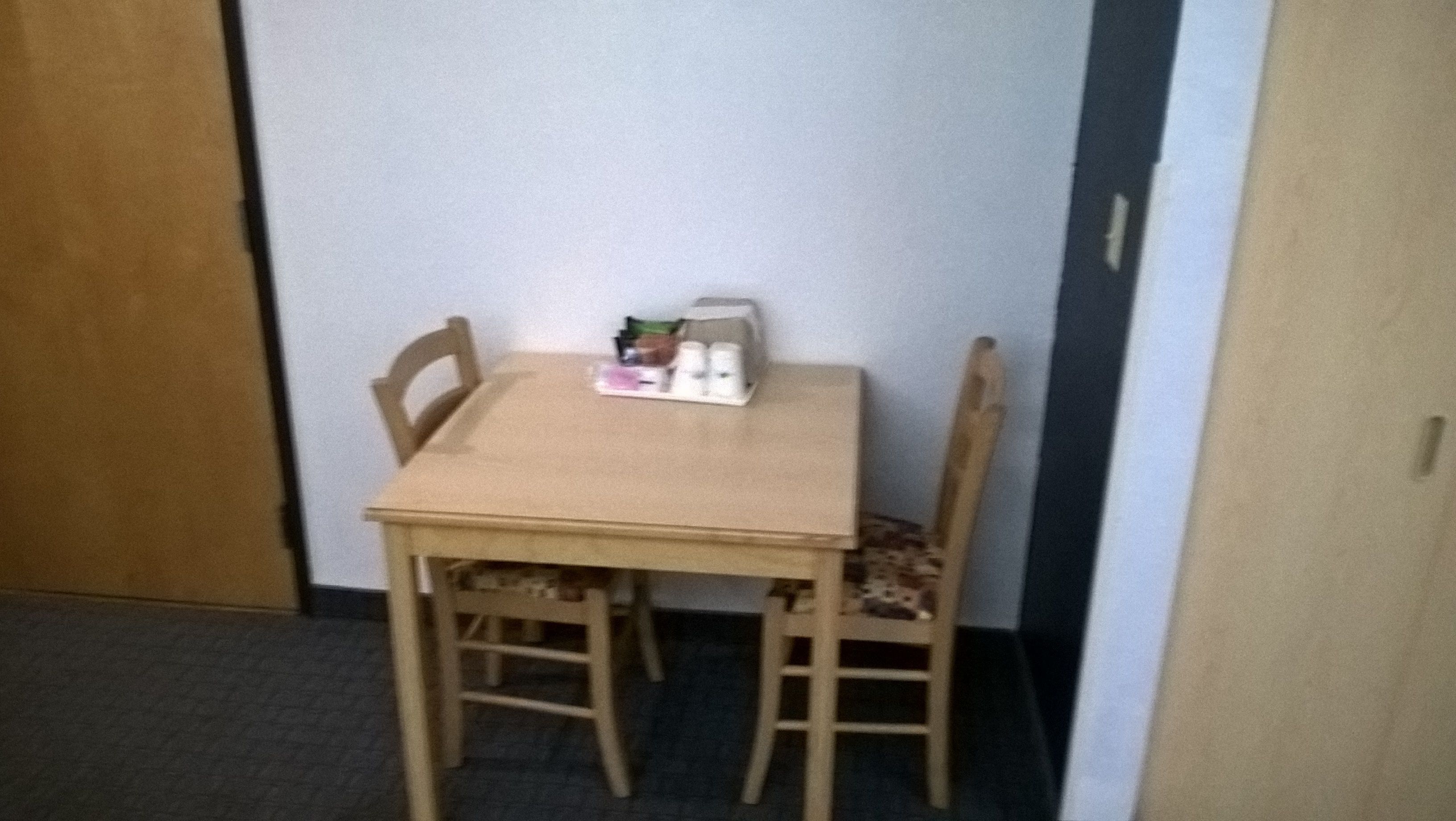 A small wooden table with two chairs, a box of tissues, and a small container of cream.