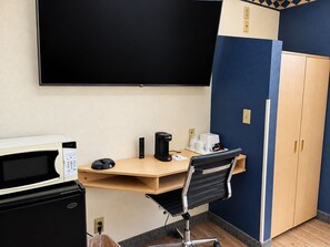 A hotel room with a desk, a microwave, a coffee maker, a chair, and a wardrobe.