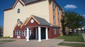 A two-story building with a red and beige facade, a central entrance with columns, and a small porch.