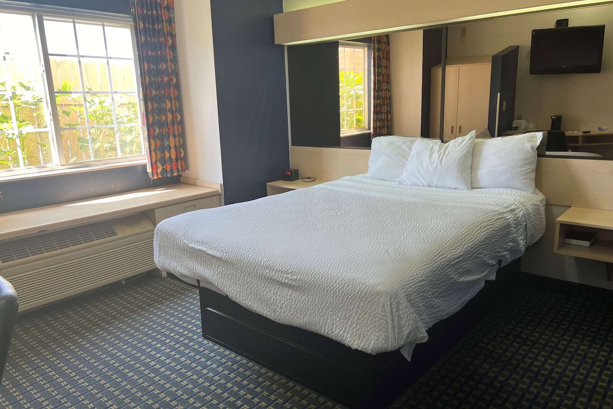 Een hotelkamer met een bed, een raam met gordijnen, een verwarming, een kleine tafel, een televisie en een spiegel.