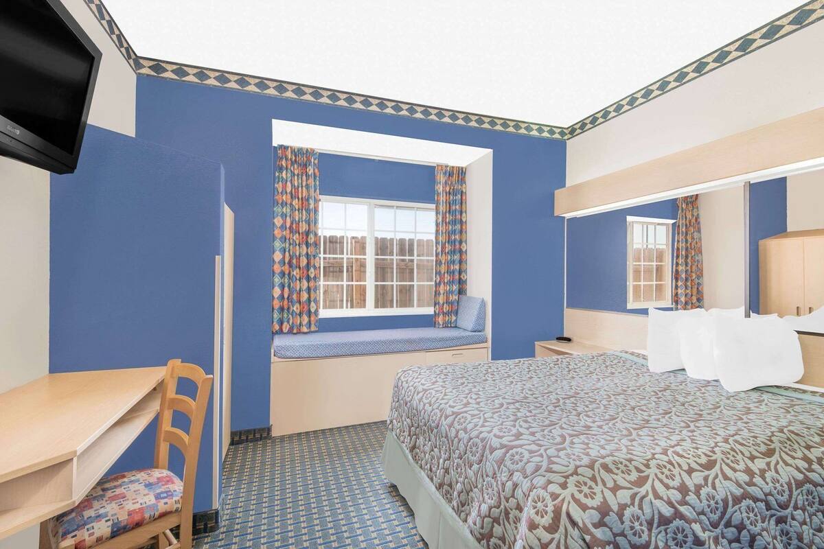 Een hotelkamer met een bed, bureau, stoel, raam met gordijnen met patroon, spiegel en televisie.