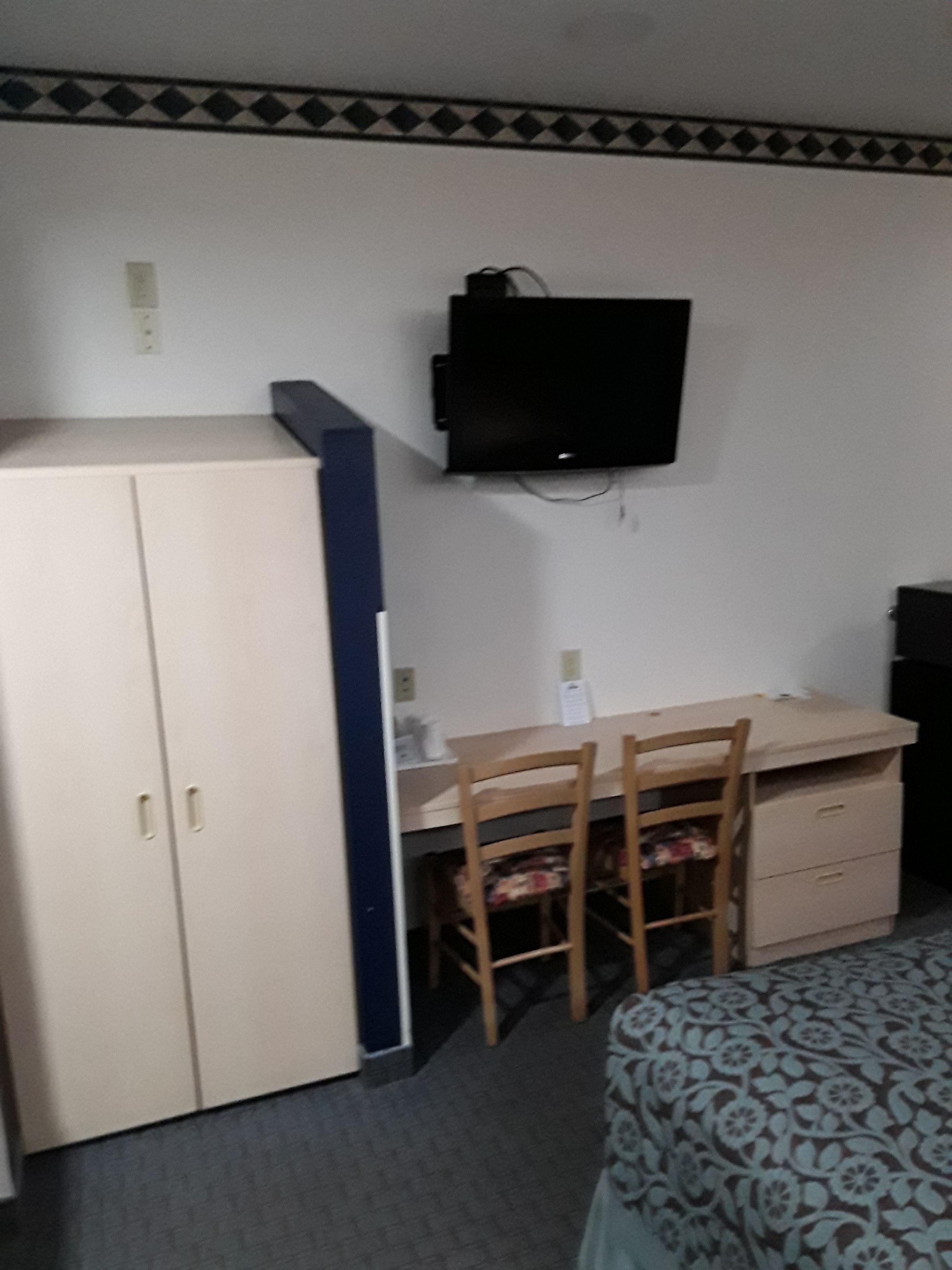 Una habitación con cama, escritorio con silla, armario y televisor montado en la pared.