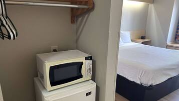 Une chambre de taille modeste, comprenant un lit, une petite table de chevet, un four à micro-ondes et un réfrigérateur.