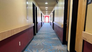 A long, narrow hallway with a patterned carpet, doors on both sides, and a red-lit end.