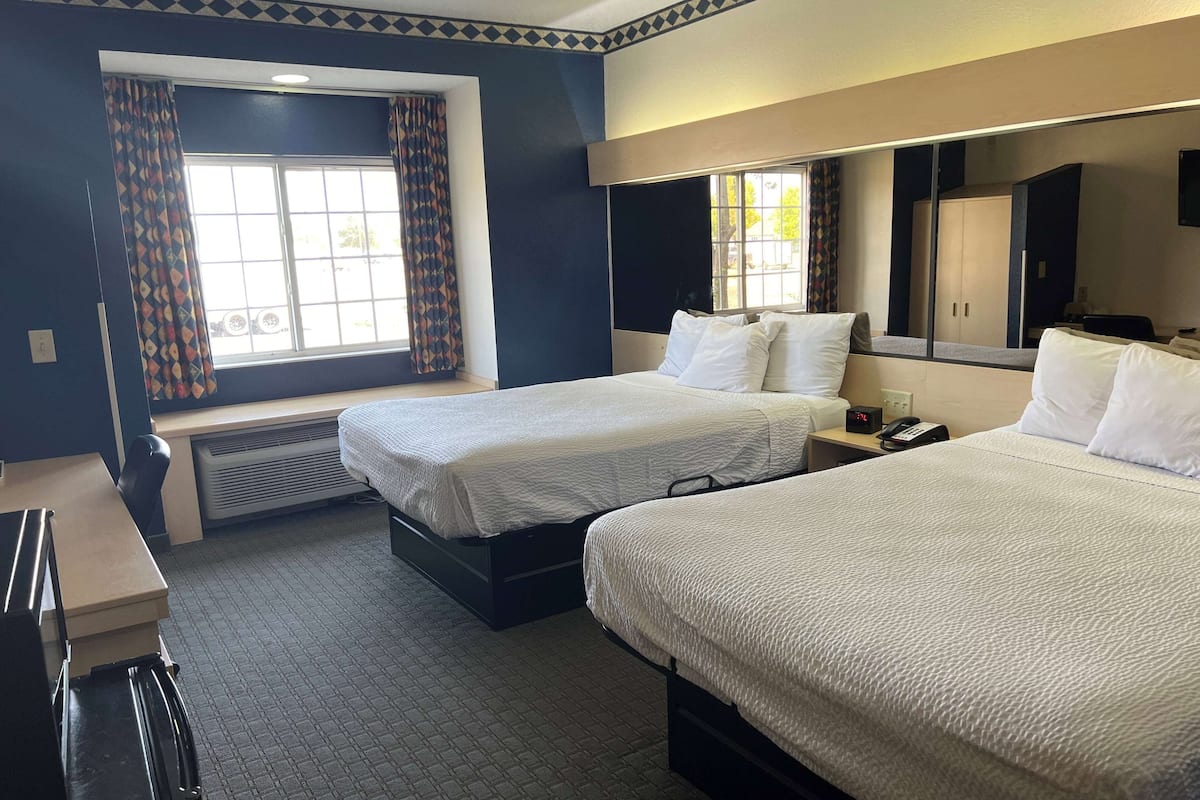 Een hotelkamer met twee bedden, een bureau, een stoel, een verwarming en een raam met gordijnen.