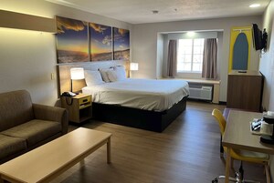 Habitación de hotel con cama, sofá, escritorio y ventana con cortinas.