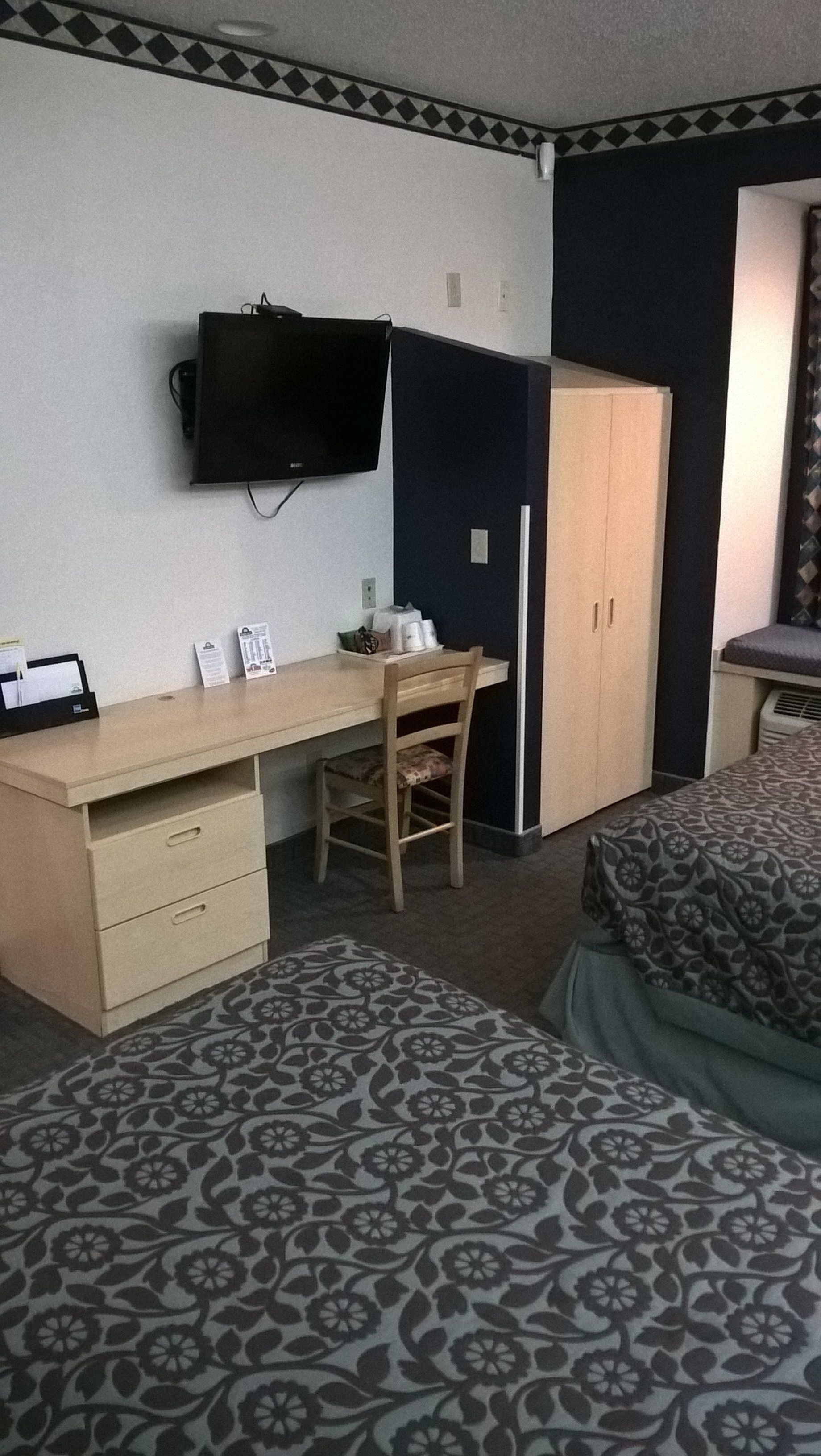 Une chambre d’hôtel comprenant un lit, un bureau avec une chaise, une armoire et un téléviseur fixé au mur.