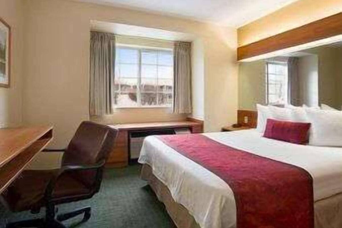 A hotel room with a bed, desk, chair, and a window with curtains.