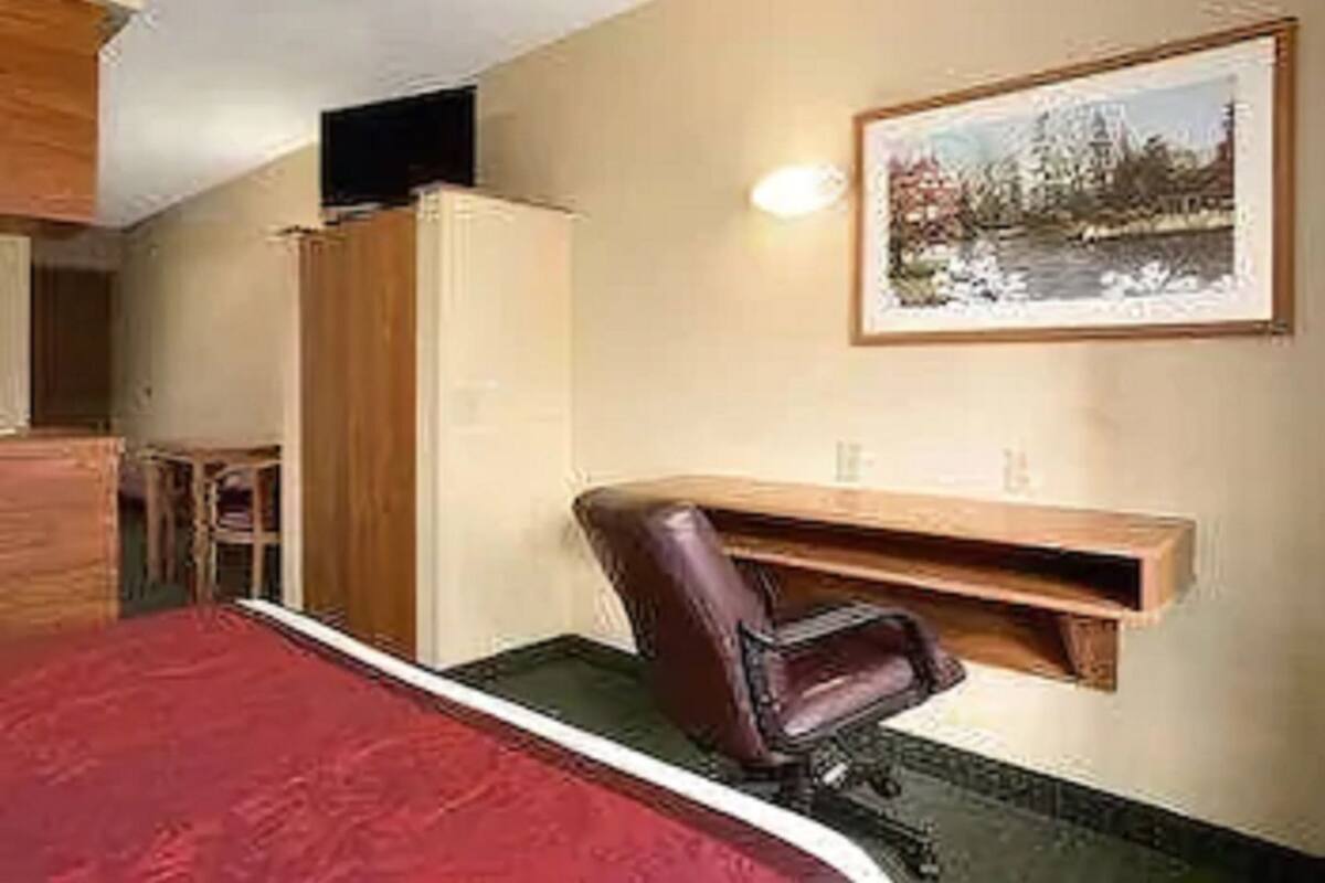 A bedroom with a bed, a desk, a chair, a wardrobe, and a framed picture on the wall.