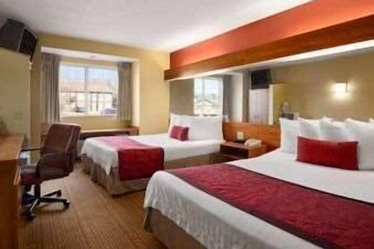A hotel room with two beds, a desk, a chair, and a window.