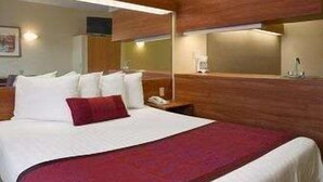A hotel room with a large bed, wooden paneling, a nightstand with a lamp, and a mirror above the bed.