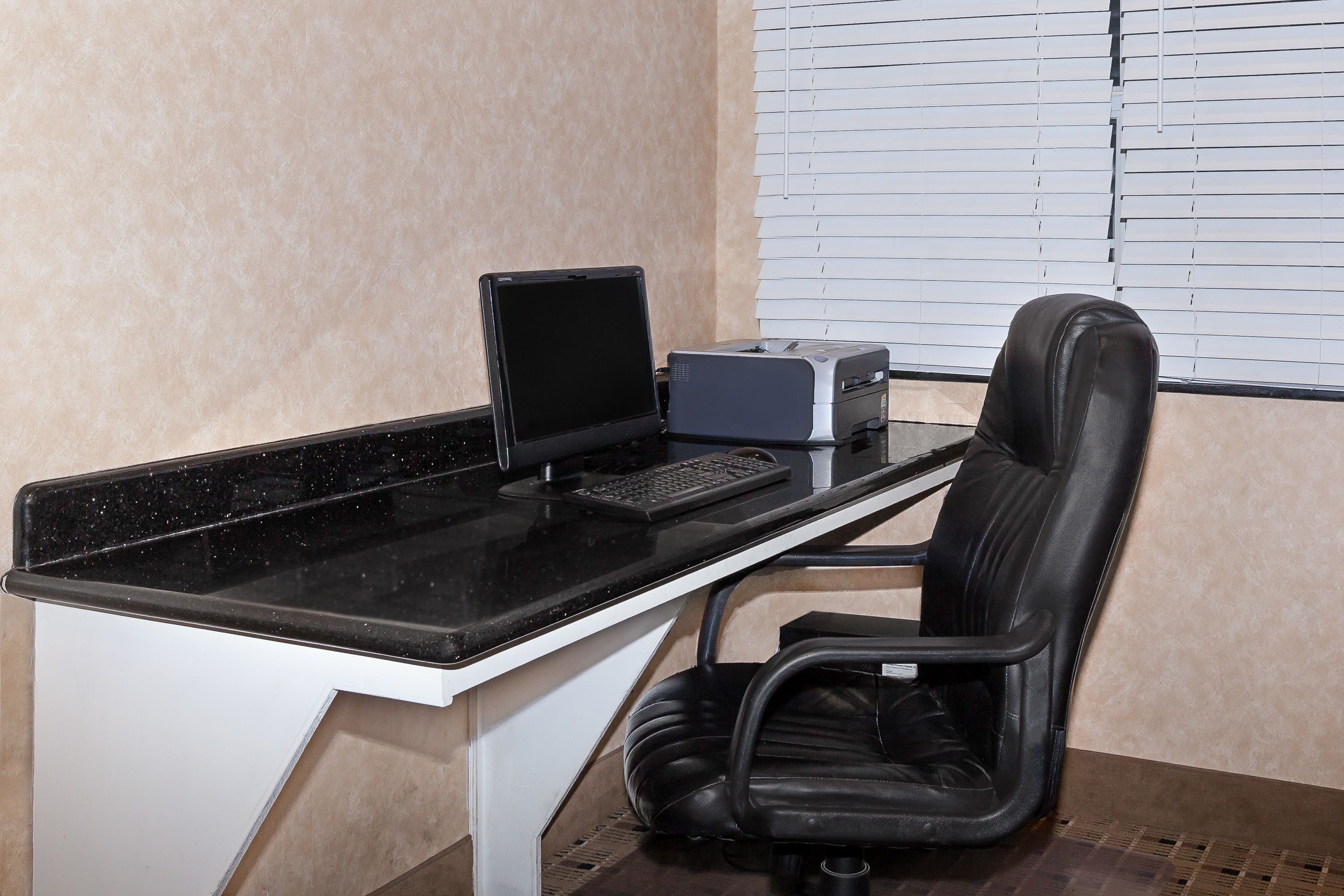 Un espace de travail comprenant un bureau noir, un écran d’ordinateur, une imprimante et une chaise de bureau noire.