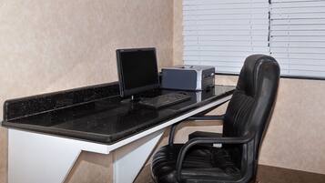 Un espace de travail comprenant un bureau noir, un écran d’ordinateur, une imprimante et une chaise de bureau noire.