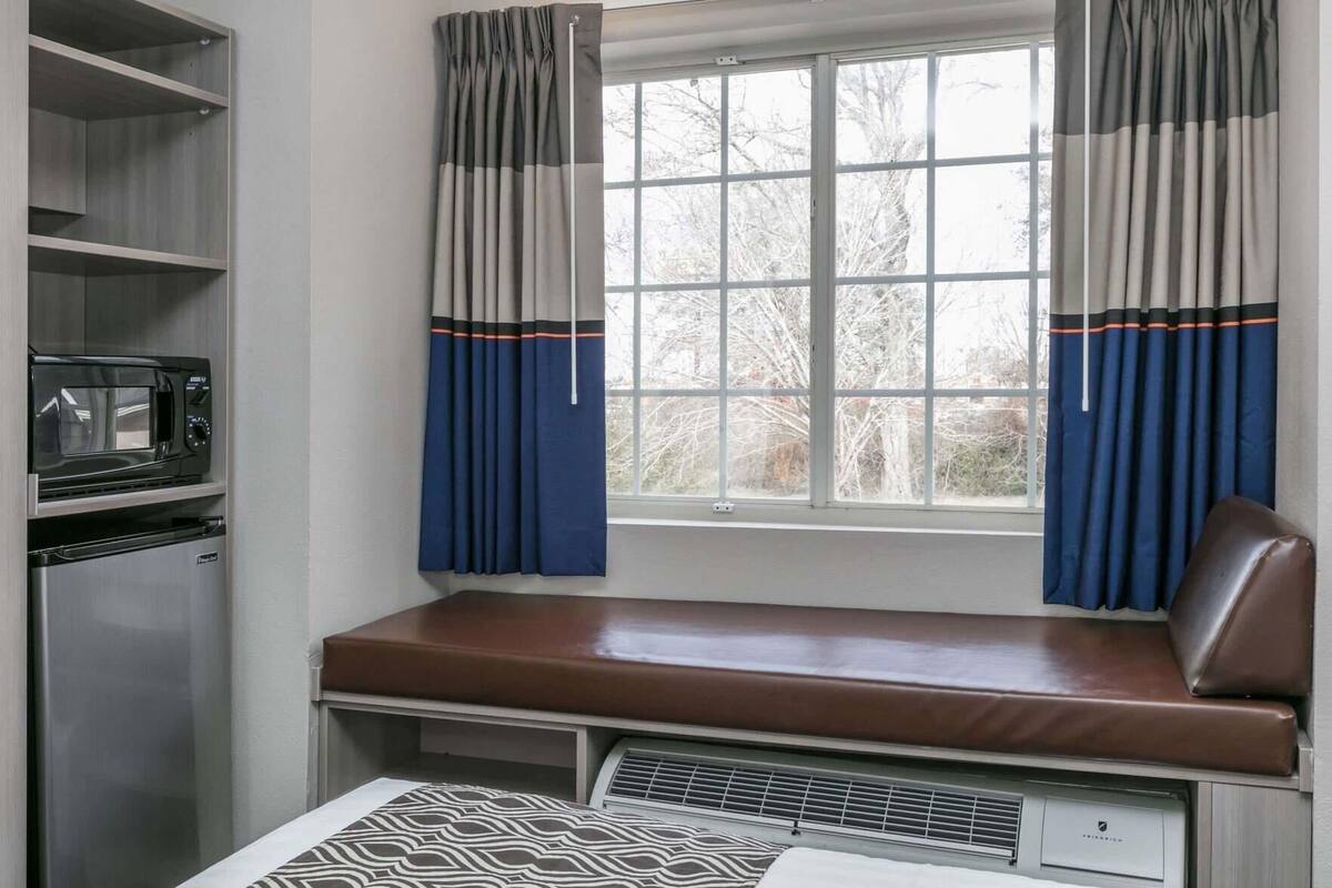A compact kitchen with a built-in microwave and refrigerator, a window with curtains, and a bench seat.