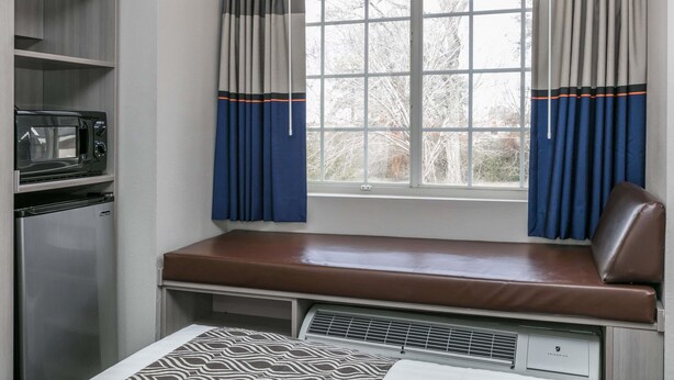 A compact room with a kitchenette, a window with curtains, and a bench with a seat. - Microtel Inn & Suites by Wyndham Scott/Lafayette (Scott)
