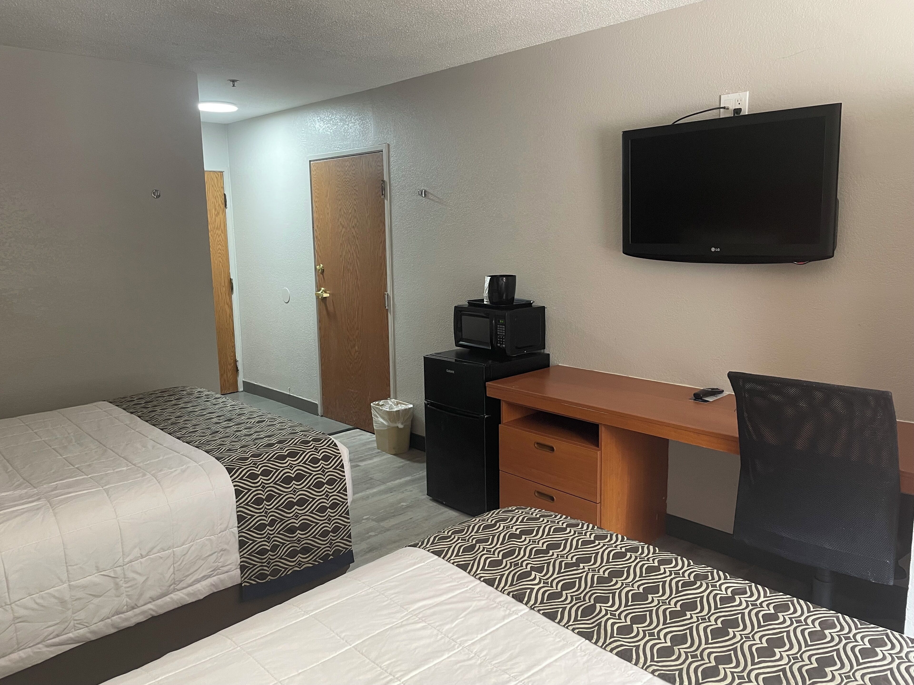 A hotel room with two beds, a desk, a chair, a television, and a microwave.