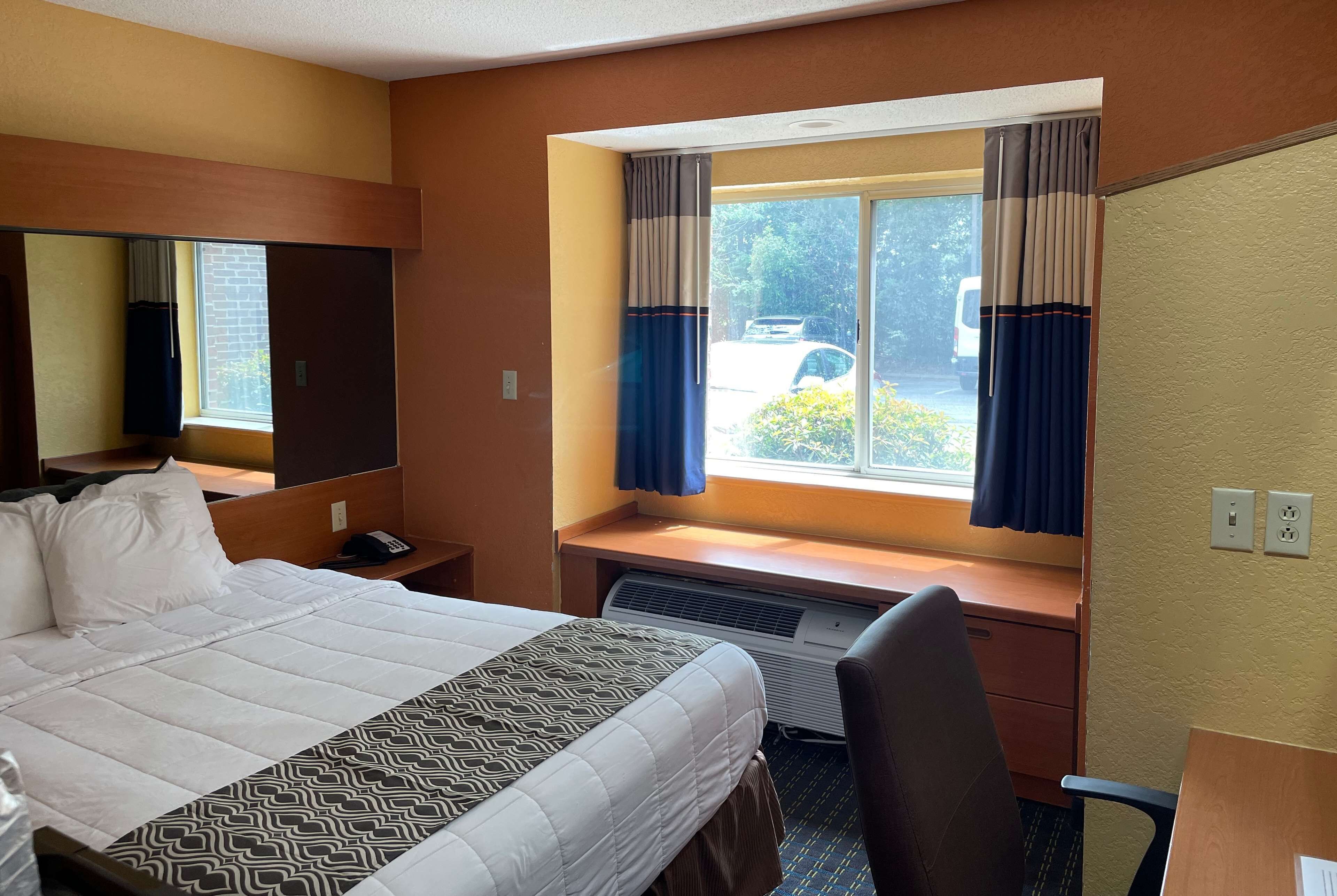 A hotel room with a bed, a desk, a chair, a window with curtains, and a view of the outside.