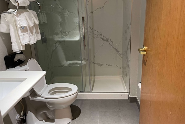 Un baño con cabina de ducha de vidrio, inodoro blanco y lavabo.