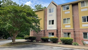 A multi-story building with a brick facade and beige accents, featuring multiple windows and a parking lot. - Microtel Inn by Wyndham Newport News Airport (Newport News)