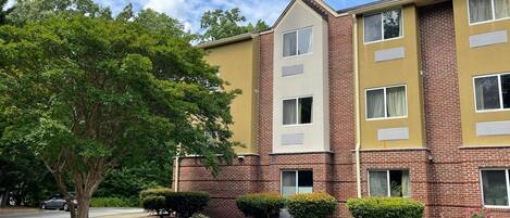 A multi-story building with a brick facade and beige accents, featuring multiple windows and a parking lot.