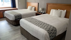 Two double beds with wooden headboards, a bedside table with a lamp, and a window with curtains. - Microtel Inn by Wyndham Newport News Airport (Newport News)