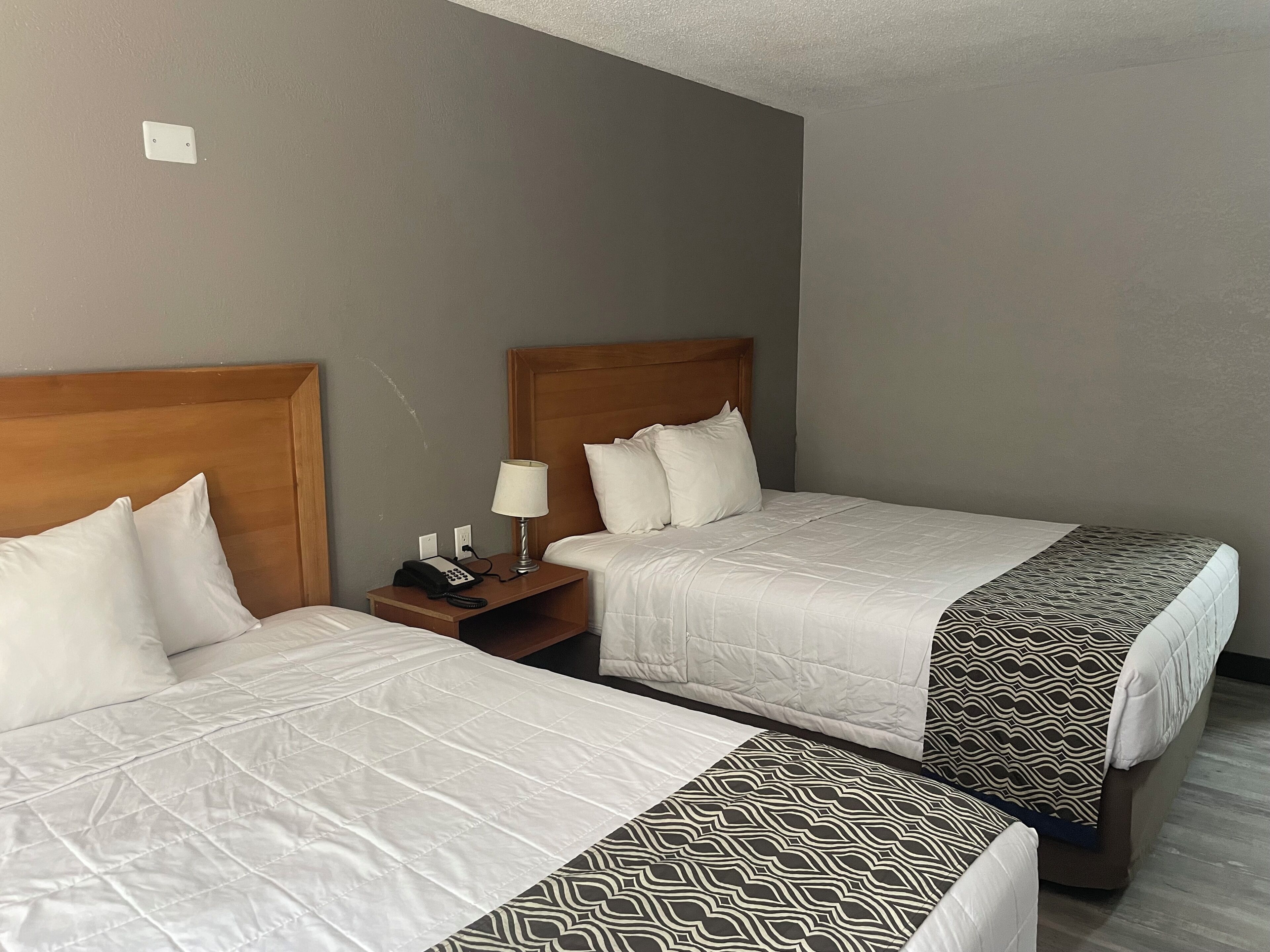 Two single beds with wooden headboards, a bedside table with a lamp, and a telephone.