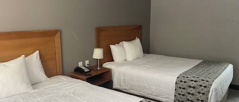 Two single beds with wooden headboards, a bedside table with a lamp, and a telephone.