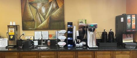 A cafe counter with a waffle iron, coffee machine, and juice dispenser.