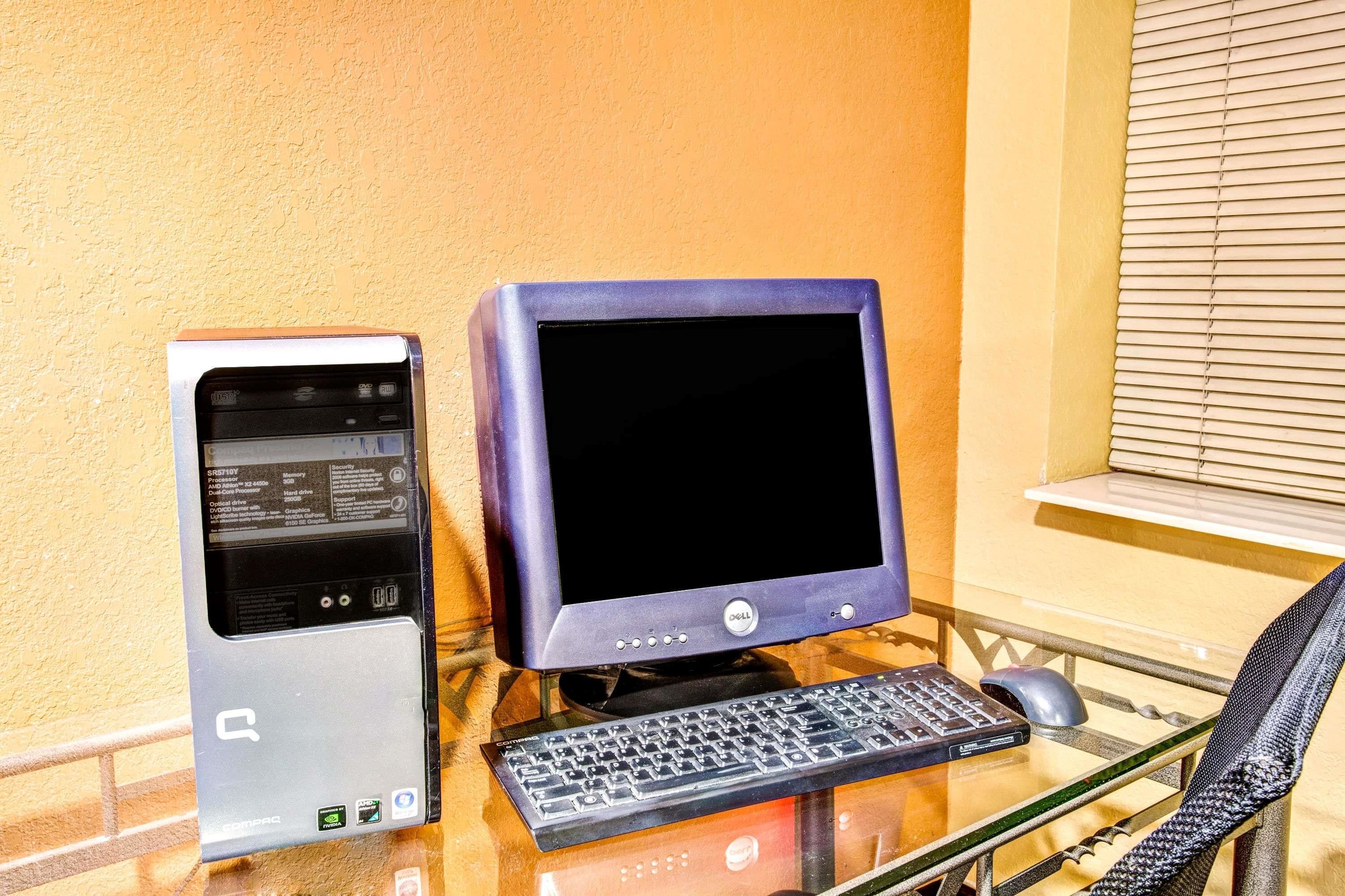 A desktop computer setup with a monitor, keyboard, and mouse on a glass table against a yellow wall.