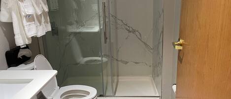 Un baño con inodoro, cabina de ducha de vidrio y lavabo con toallero.