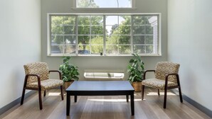 Una habitación con un gran ventanal arqueado, dos sillones, una mesa y plantas en macetas.