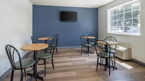Una habitación con pared azul, un televisor montado y un amplio ventanal con vista a coches estacionados.