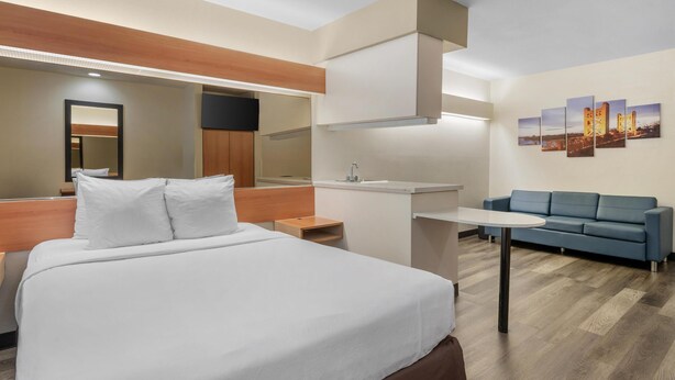 Habitación de hotel con cama, escritorio, sofá, espejo y una pared decorada con obras de arte.
