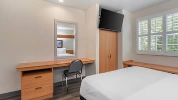 A bedroom with a bed, a desk, a chair, a wardrobe, and a TV.