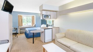 A compact room with a bed, a small kitchenette, a sofa, and a television mounted on the wall.