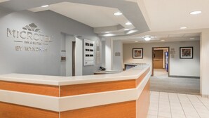A reception desk with a wooden accent, a grey wall with the Microtel Inn & Suites logo, and a hallway leading to other areas.