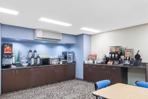 Una kitchenette con microondas, cafetera y diversos alimentos. Hay una mesa y sillas en la habitación.