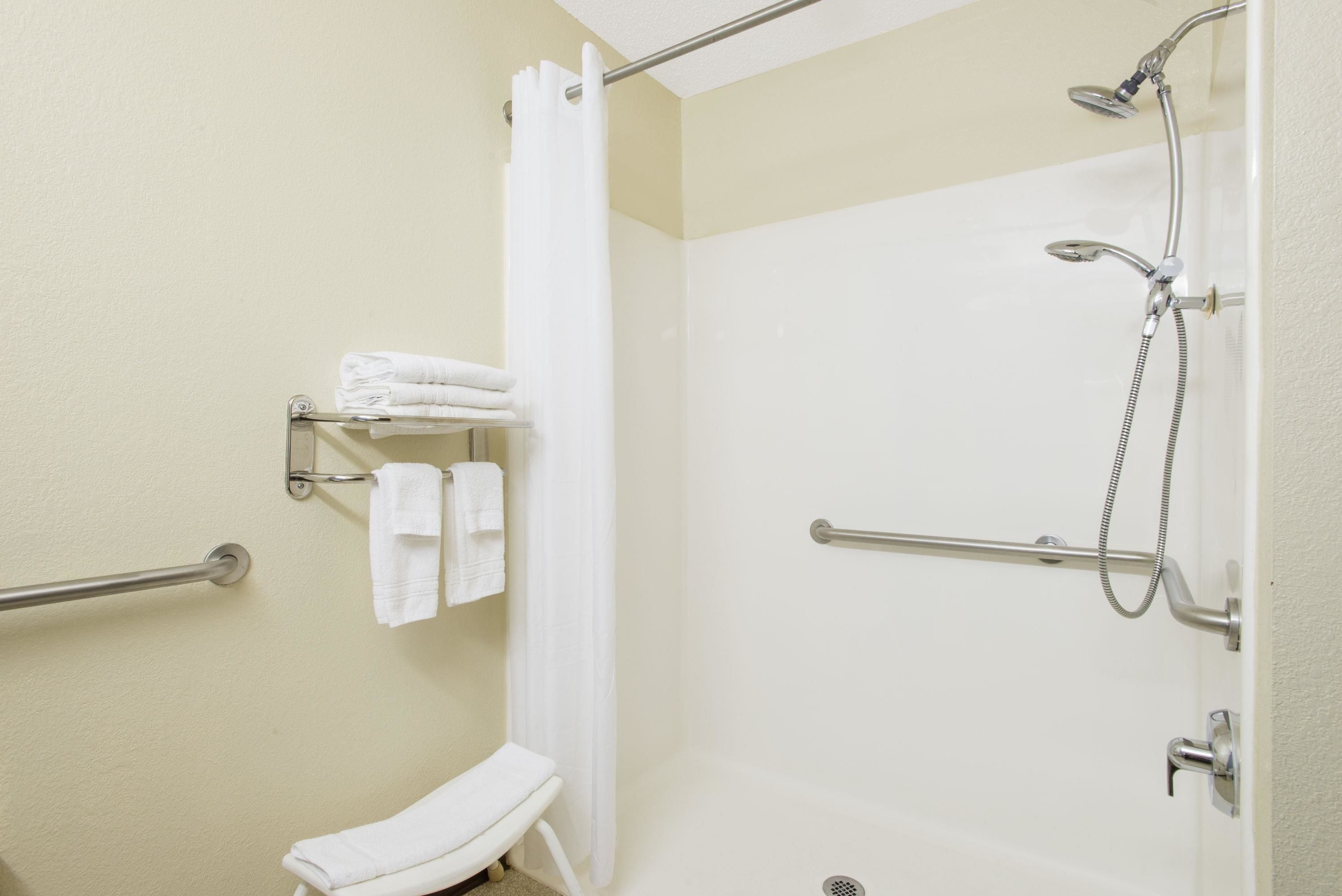 A bathroom with a shower, grab bars, a toilet, and a towel rack.