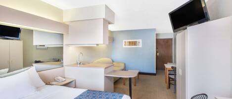 A hotel room with a bed, a desk, a chair, a TV, and a bathroom.